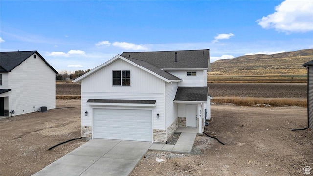 view of front of house with concrete driveway, a mountain view, stone siding, an attached garage, and a shingled roof