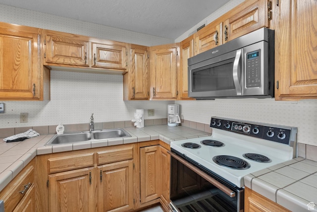 kitchen featuring a sink, a textured ceiling, stainless steel microwave, wallpapered walls, and white electric stove
