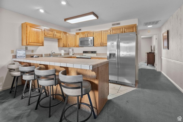 kitchen featuring visible vents, a peninsula, tile counters, a sink, and stainless steel appliances