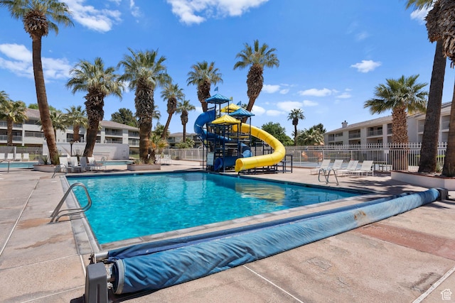 community pool with fence, a water slide, playground community, and a patio area