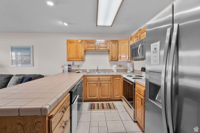 kitchen with appliances with stainless steel finishes, a sink, tile countertops, a peninsula, and light tile patterned floors