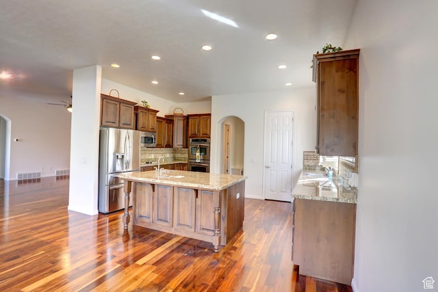 kitchen featuring arched walkways, a ceiling fan, stainless steel appliances, decorative backsplash, and light stone counters