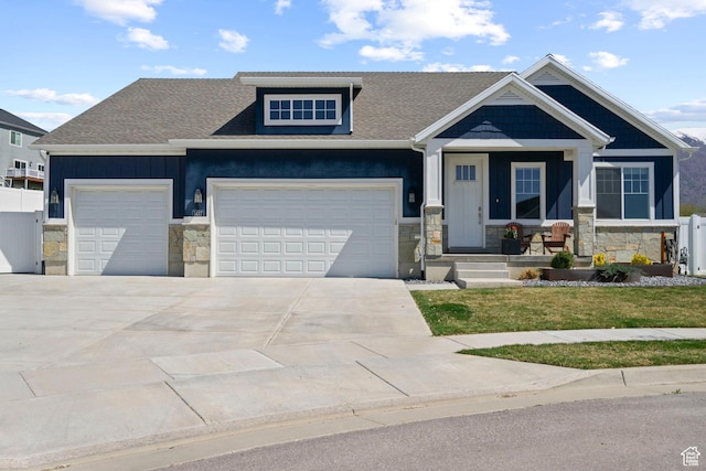 craftsman-style home with covered porch, stone siding, an attached garage, a shingled roof, and driveway