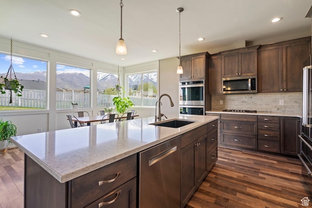 kitchen featuring hanging light fixtures, a sink, dark wood-style flooring, appliances with stainless steel finishes, and backsplash