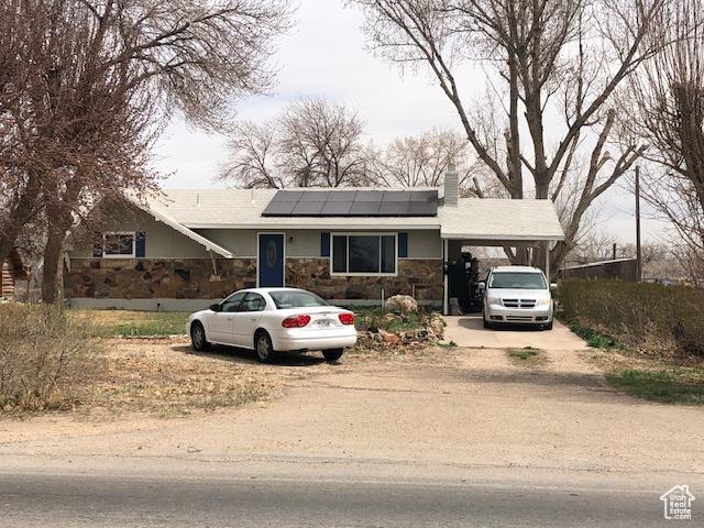 view of front of home featuring a chimney, dirt driveway, stone siding, an attached carport, and solar panels