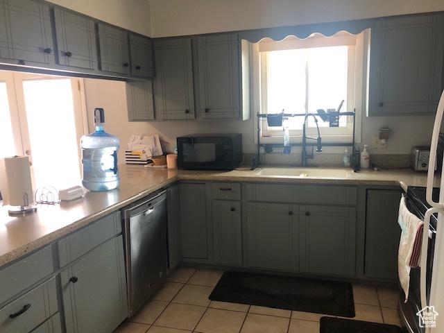 kitchen with black microwave, light tile patterned floors, light countertops, dishwasher, and a sink