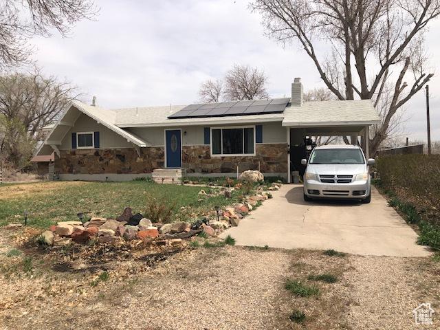 single story home with solar panels, a carport, stone siding, a chimney, and concrete driveway