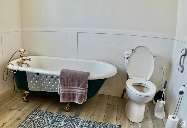 3193 S Southfield Rd W, Daniel, UT 84032 - bathroom with toilet, tile walls, a soaking tub, wood finished floors, and a wainscoted wall
