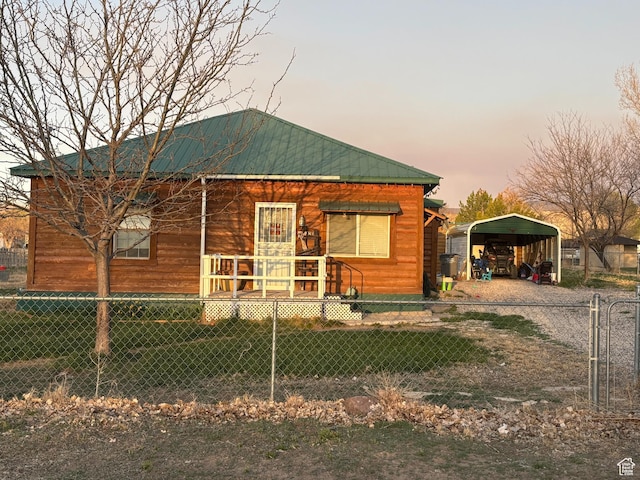 bungalow-style house with a carport, metal roof, fence, and dirt driveway