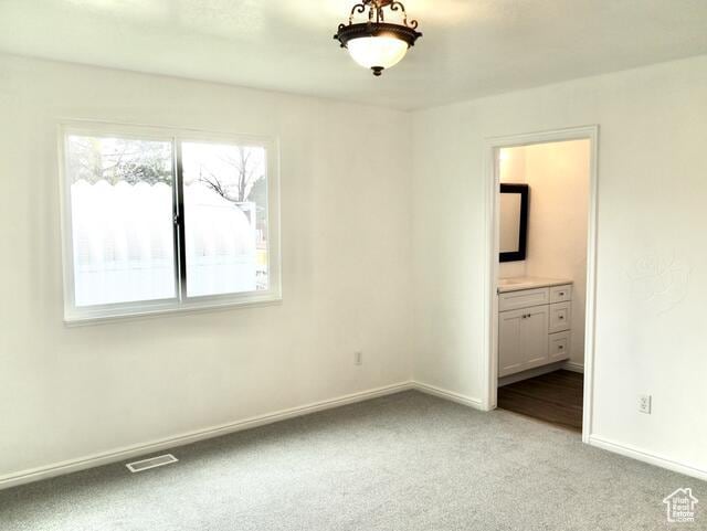unfurnished bedroom with ensuite bath, visible vents, baseboards, and light colored carpet
