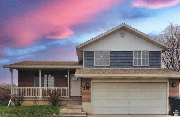 tri-level home featuring concrete driveway, covered porch, an attached garage, brick siding, and roof mounted solar panels