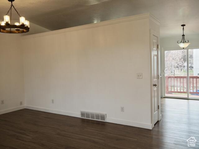 spare room featuring a notable chandelier, dark wood-type flooring, visible vents, and baseboards