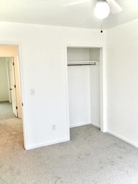unfurnished bedroom featuring a closet, light colored carpet, ceiling fan, and baseboards