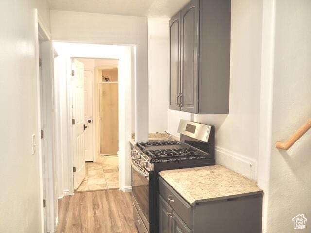 kitchen featuring baseboards, light wood-type flooring, gray cabinetry, and stainless steel range with gas cooktop