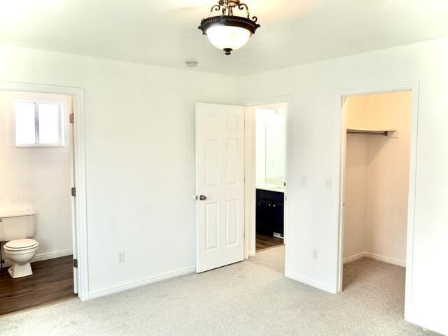 unfurnished bedroom featuring baseboards, a closet, ensuite bath, and a walk in closet