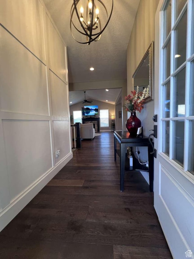 hall with dark wood-style floors, an inviting chandelier, vaulted ceiling, baseboards, and a textured ceiling
