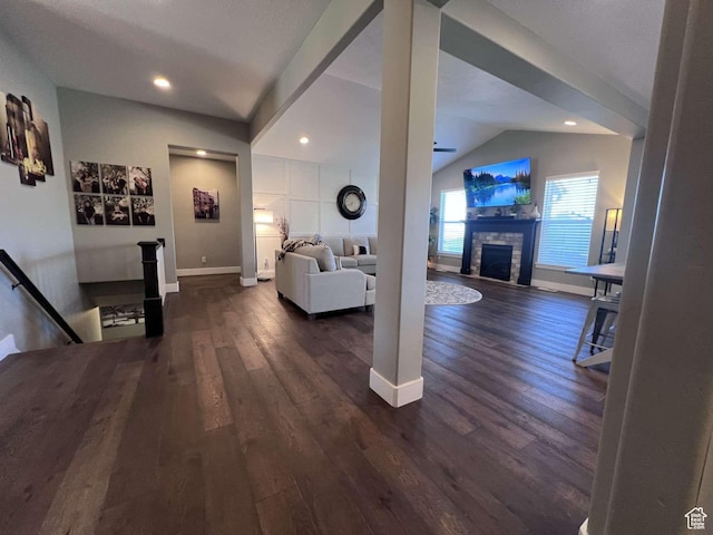 living area with dark wood finished floors, vaulted ceiling, baseboards, recessed lighting, and a stone fireplace