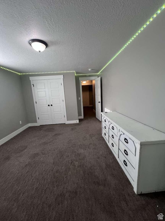 unfurnished bedroom featuring dark carpet, baseboards, a textured ceiling, and a closet