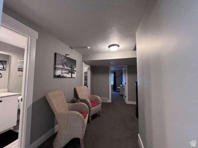 hallway featuring baseboards, dark colored carpet, a textured ceiling, and visible vents