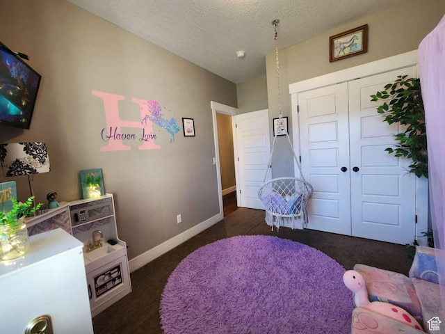 bedroom with a textured ceiling, dark carpet, a closet, and baseboards