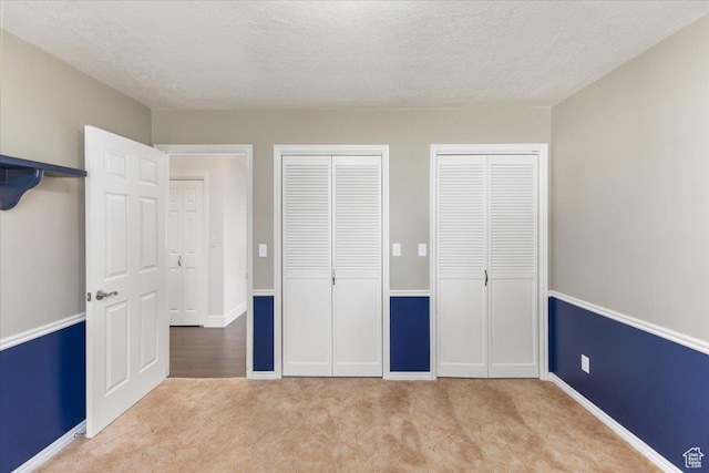 unfurnished bedroom with a textured ceiling, carpet flooring, baseboards, and multiple closets