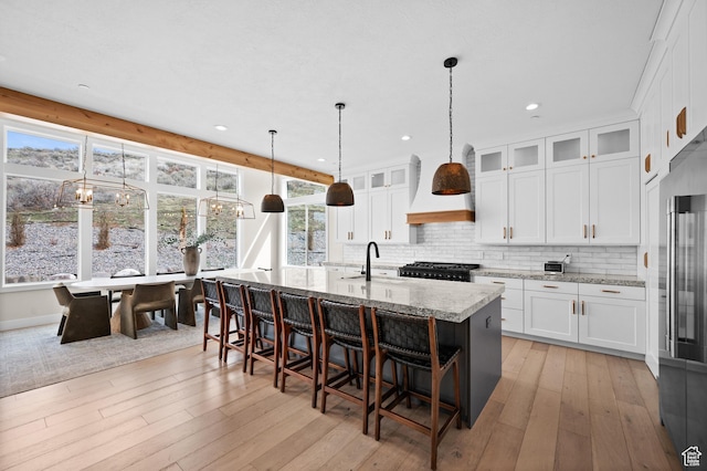 kitchen featuring stove, light wood-style flooring, white cabinetry, backsplash, and a center island with sink