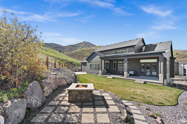 rear view of house featuring french doors, a patio area, an outdoor fire pit, a mountain view, and a yard