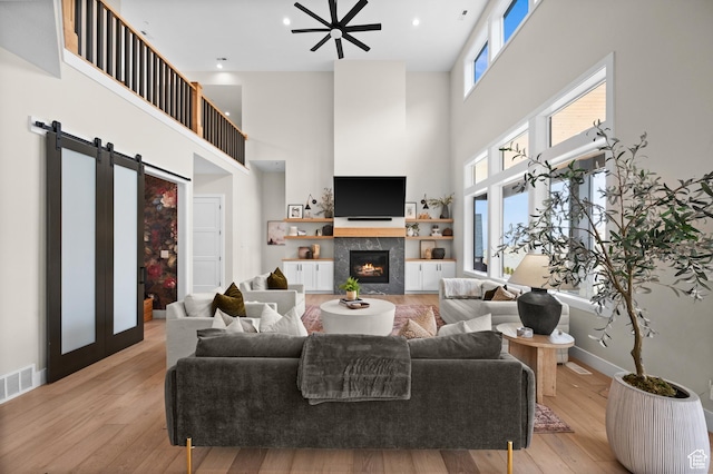 living area with visible vents, a fireplace, light wood finished floors, and a towering ceiling