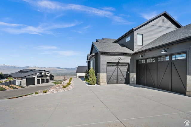 view of home's exterior with an attached garage, roof with shingles, a mountain view, and driveway
