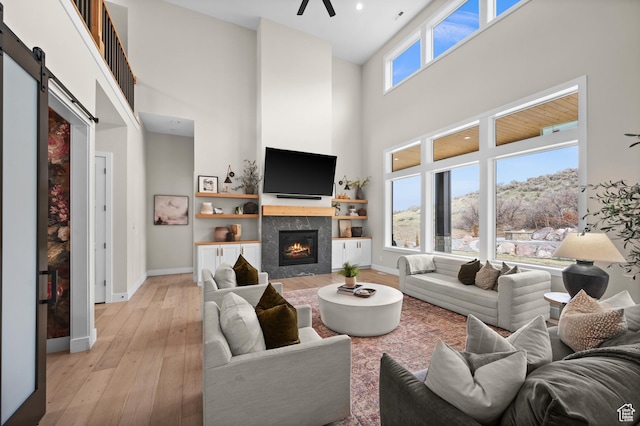 living area featuring a barn door, a ceiling fan, a tile fireplace, and a towering ceiling