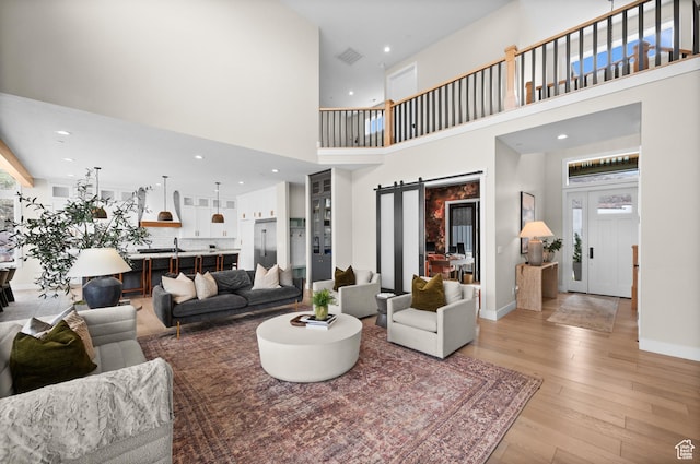 living room with visible vents, light wood-type flooring, a barn door, a high ceiling, and recessed lighting