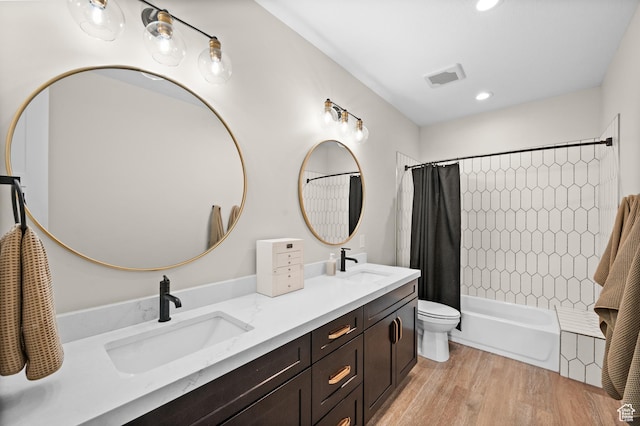 full bath with double vanity, visible vents, a sink, and wood finished floors