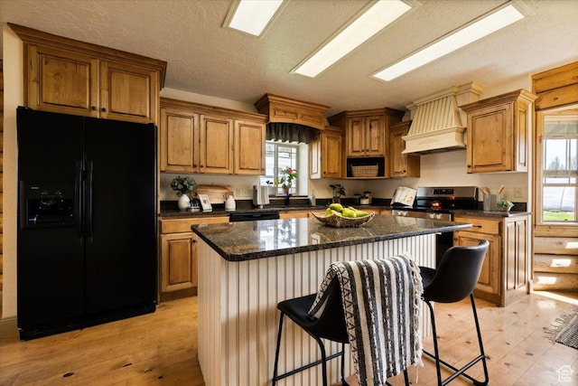 kitchen featuring brown cabinets, custom range hood, light wood-style flooring, and black appliances