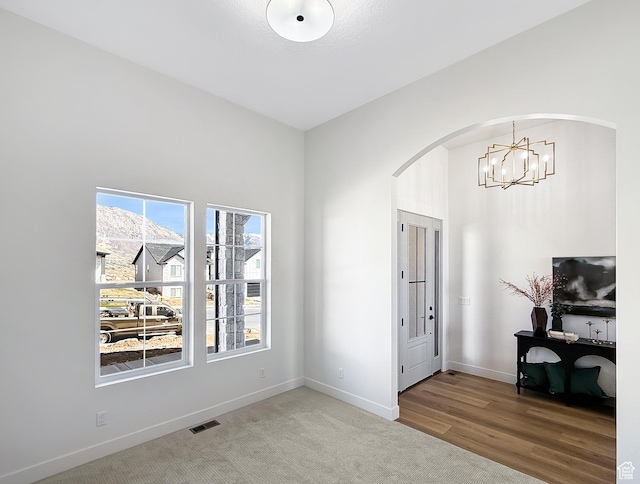 carpeted entryway with visible vents, arched walkways, an inviting chandelier, and a healthy amount of sunlight