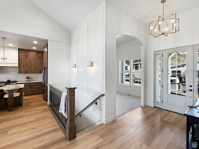 foyer entrance featuring a notable chandelier, baseboards, high vaulted ceiling, arched walkways, and light wood finished floors