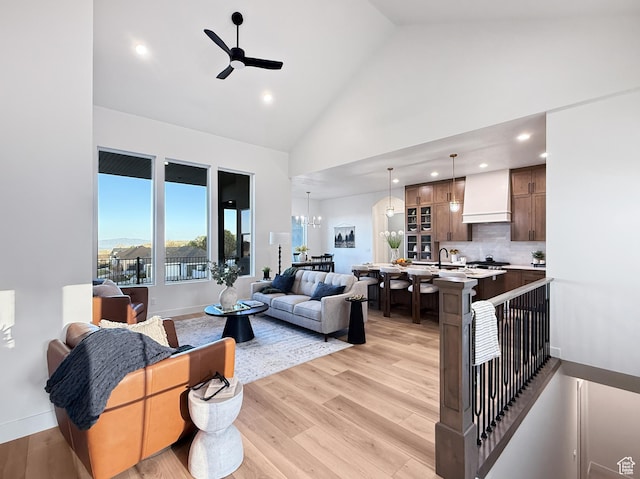 living room with ceiling fan with notable chandelier, high vaulted ceiling, light wood-style flooring, recessed lighting, and baseboards