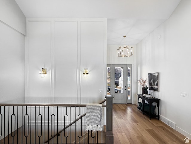 hall featuring baseboards, an inviting chandelier, an upstairs landing, visible vents, and wood finished floors