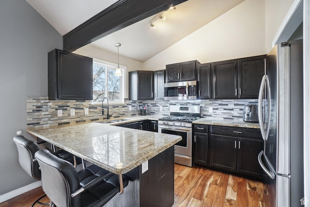 kitchen with a peninsula, a sink, lofted ceiling, a breakfast bar, and appliances with stainless steel finishes
