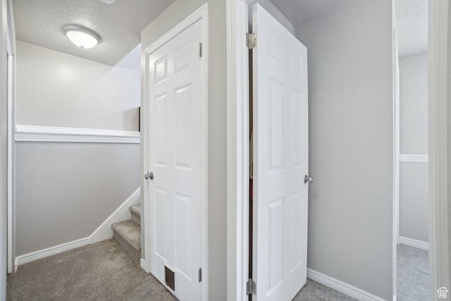 hall featuring baseboards, carpet, and a textured ceiling