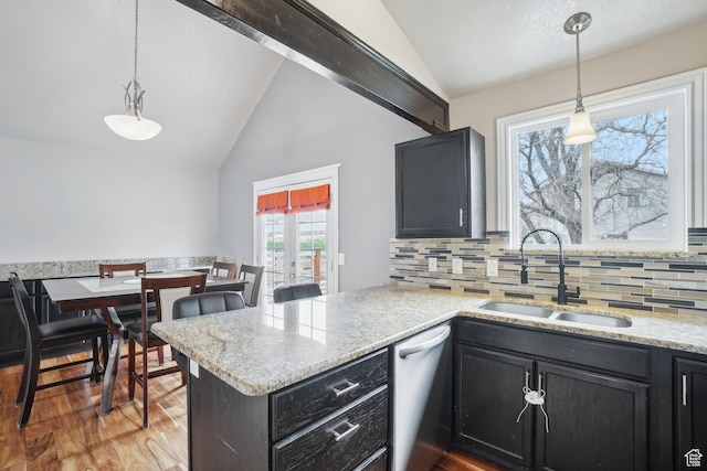 kitchen with a peninsula, stainless steel dishwasher, a sink, lofted ceiling, and decorative backsplash