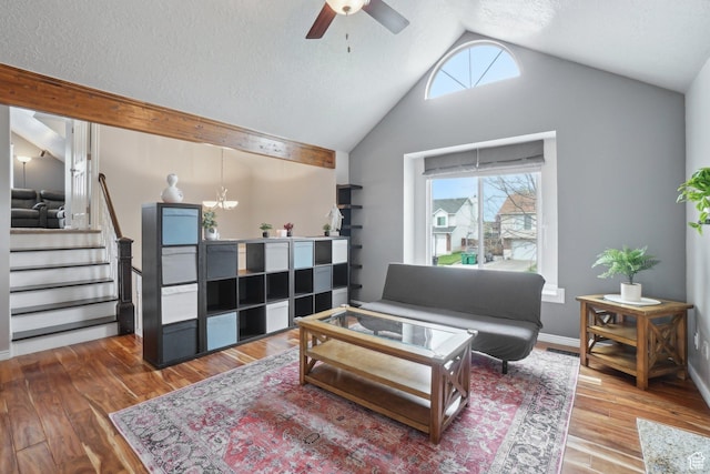 living room featuring stairway, high vaulted ceiling, wood finished floors, a textured ceiling, and ceiling fan with notable chandelier