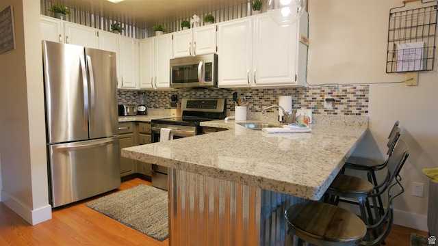 3615 N Wolf Lodge Dr Unit 211, Eden, UT 84310 - kitchen featuring light stone counters, a sink, light wood-style flooring, a peninsula, and appliances with stainless steel finishes