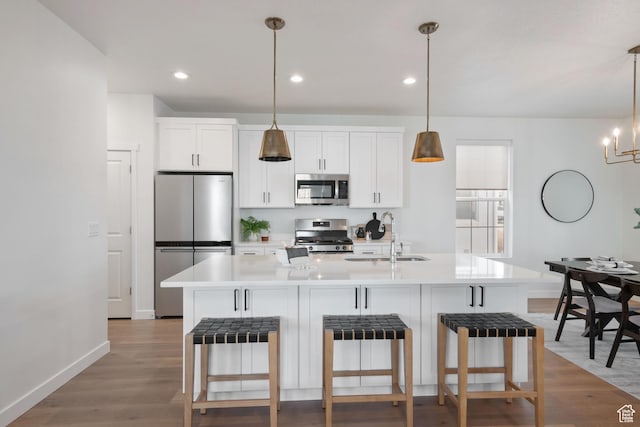 kitchen with an island with sink, white cabinets, light countertops, a sink, and stainless steel appliances