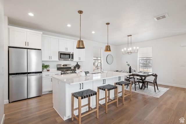 kitchen featuring stainless steel appliances, white cabinets, light wood-type flooring, and a kitchen bar