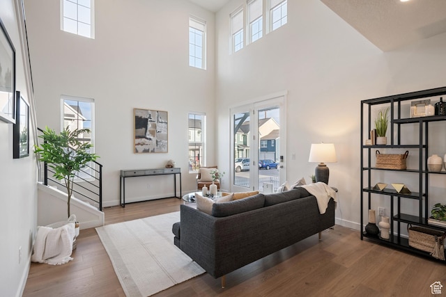 living area featuring a towering ceiling, baseboards, and wood finished floors