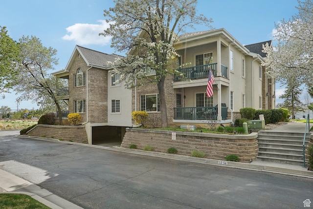 view of front facade featuring brick siding, a balcony, and stucco siding