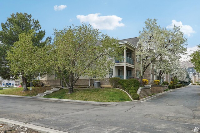 view of side of home with brick siding, central AC, a lawn, and a balcony