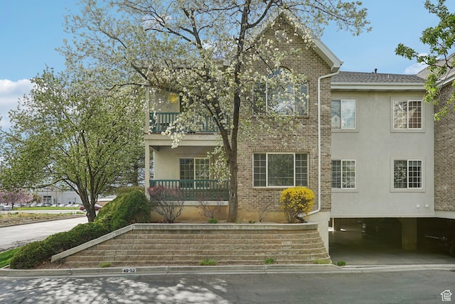 view of front facade with brick siding, stucco siding, a carport, and a balcony