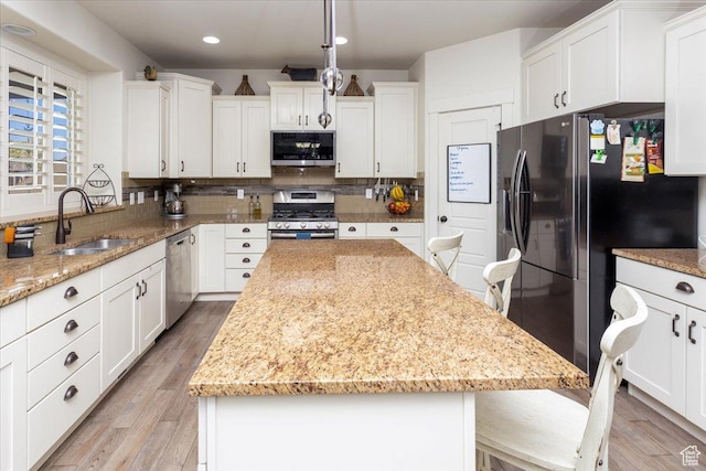 kitchen featuring white cabinetry, a kitchen island, light stone countertops, appliances with stainless steel finishes, and a sink