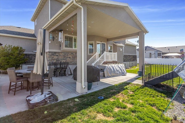 rear view of house featuring fence, stone siding, a patio, and stucco siding